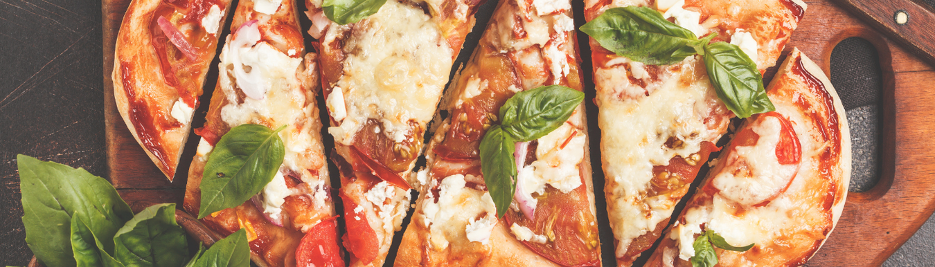 overhead shot of cheese tomato and basil pizza sliced on wooden board