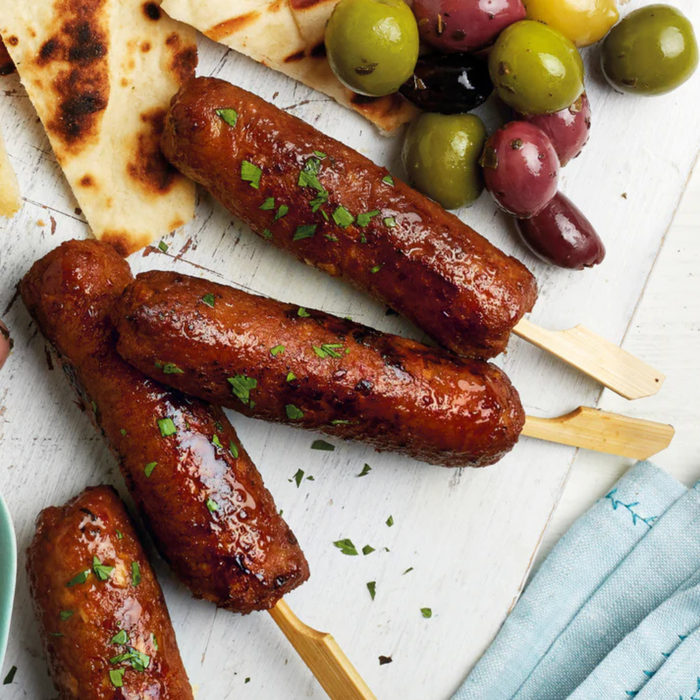 Skewered kofta on a white surface with bread and olives.