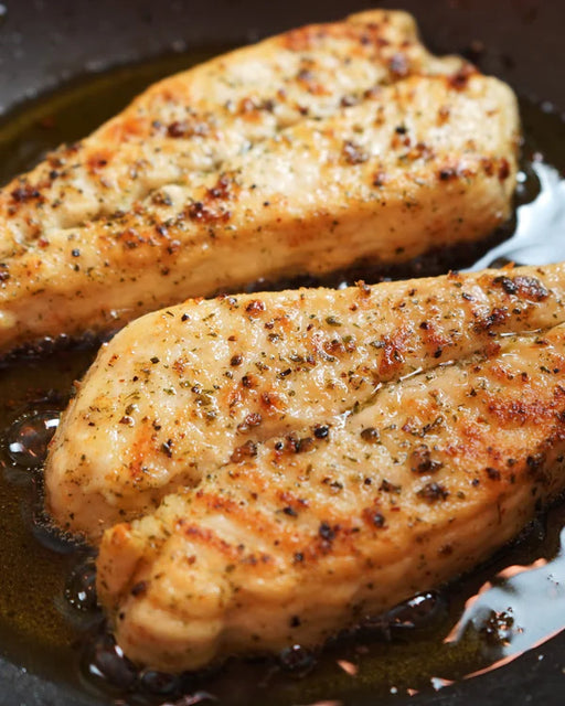 Two pieces of seared chicken breast in a frying pan.