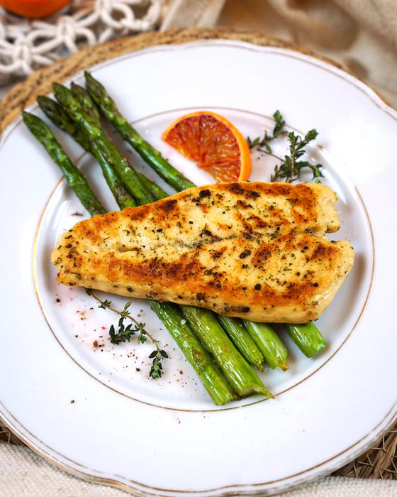 Plated dish with grilled chicken, asparagus, and blood orange slices on a white plate.
