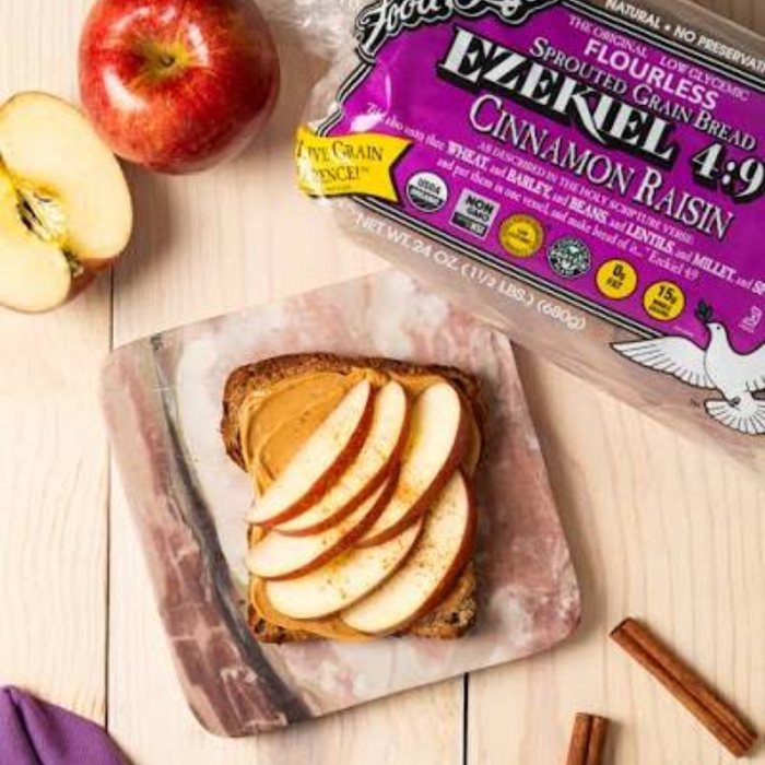 Ezekiel 4:9 cinnamon raisin bread slice with sliced appled on a breadboard with the packet and apples in the background