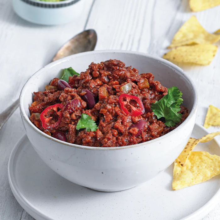 Bowl of vegan chili with tortilla chips on a white surface