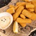 Fried fish fingers with a side of dipping sauce on a newspaper background