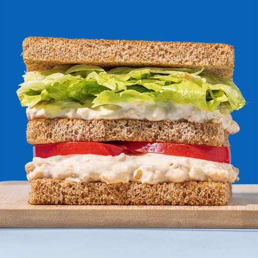 Sandwich with lettuce, tomato, and a creamy plant based tuna filling on a blue background