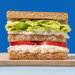 Sandwich with lettuce, tomato, and a creamy plant based tuna filling on a blue background