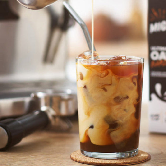 Glass of iced coffee with a blurred coffee machine and milk in the background