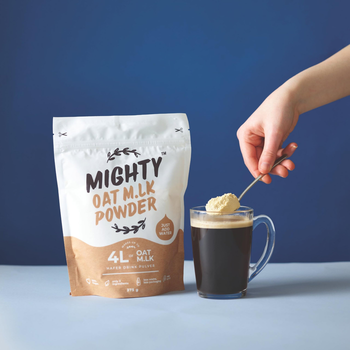 Mighty Oat M.L.K Powder package with a hand stirring a cup of coffee.