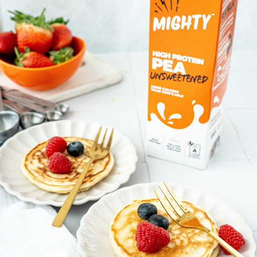 Pancakes with berries on plates next to a carton of Mighty High Protein Pea Unsweetened milk.