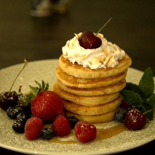 Stack of pancakes with whipped cream and berries on a decorative plate