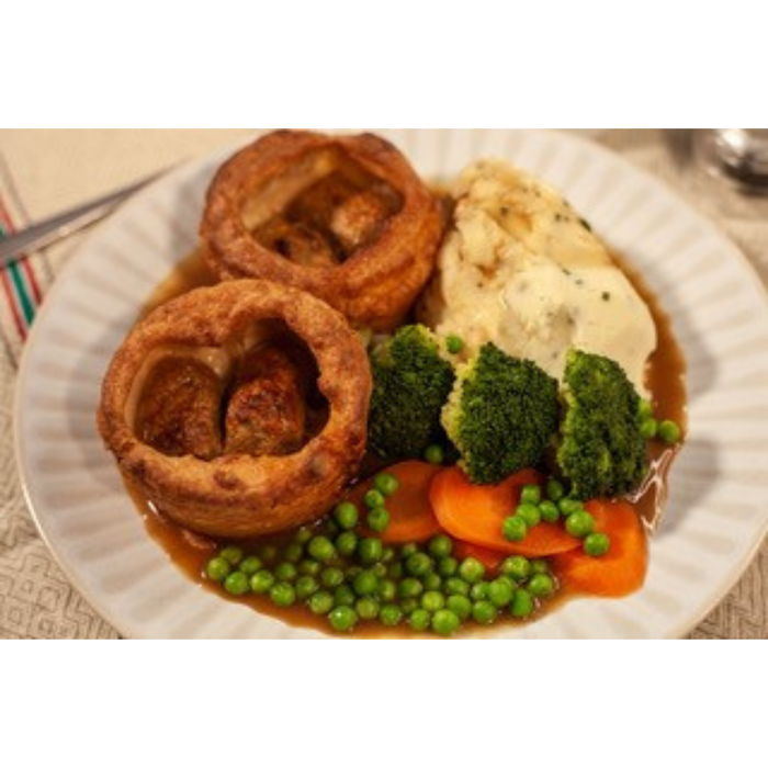 Plated dish with roasted meat, vegetables, and Yorkshire pudding on a white plate.