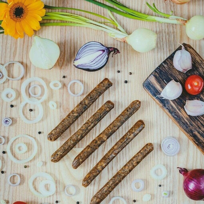 onion and garlic kabanos sausages on a wooden table surrounded by rings of onions, and cloves of garlic