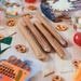 Four cheese sausages arranged on a wooden table with scattered pretzels, cheese wedges, and other snack props. A package of cheese sausages is visible in the lower left corner.