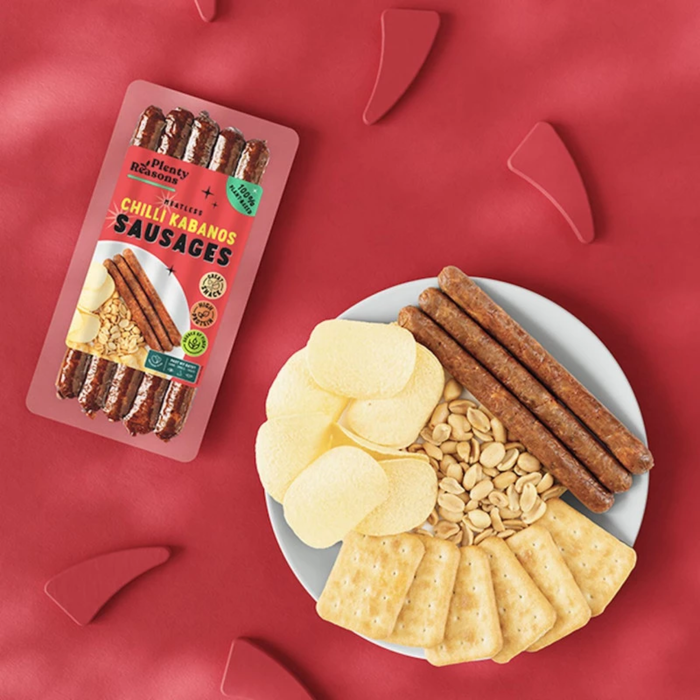 packet of chilli kabanos sausages on a red background with a plate of crisps crackers and peanuts
