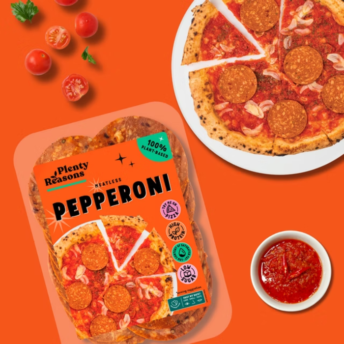 Packaged pepperoni pizza slices in a clear clamshell package labeled Plenty Reasons Pepperoni, shown on an orange background with a prepared pizza on a plate, cherry tomatoes, basil, and a small bowl of red sauce.
