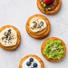 Five sweet potato hash browns with different toppings on a light gray background