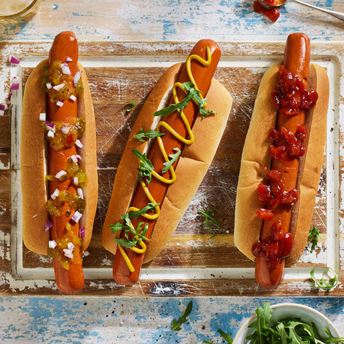 Three hot dogs with various condiments on a rustic wooden board.
