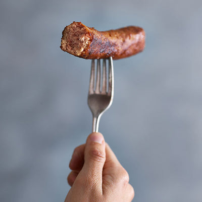 hand holding half eaten vegan sausage on a fork
